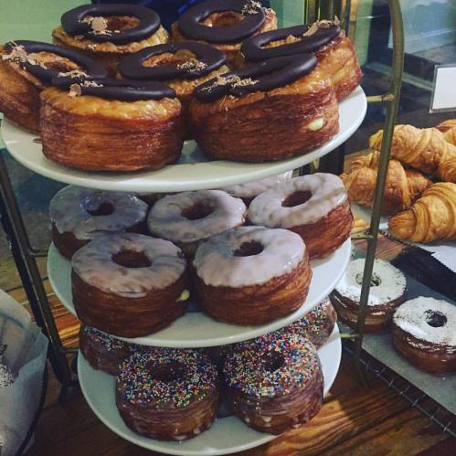 A tiered display of various donuts, including chocolate-covered and glazed, alongside croissants.