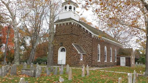 Historic stone church surrounded by autumn trees and a graveyard, with fallen leaves on the ground.