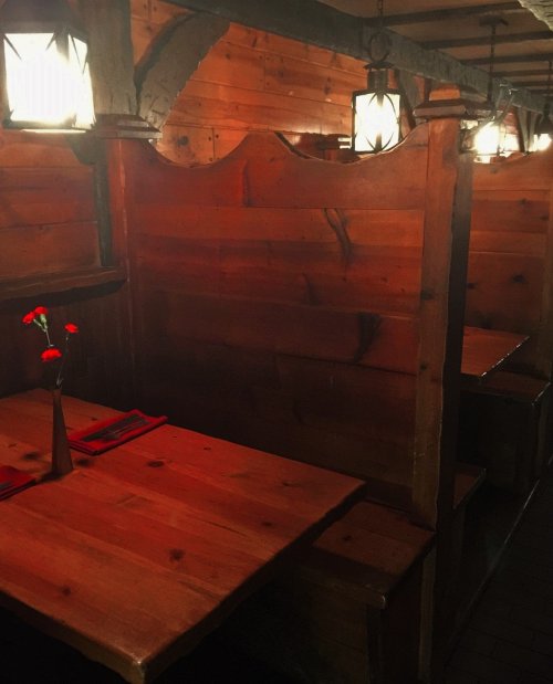 Cozy wooden restaurant interior with lanterns, featuring intimate booths and a small vase with a red flower on a table.