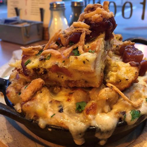 A skillet filled with cheesy macaroni topped with crispy onions and a slice of savory bread pudding.