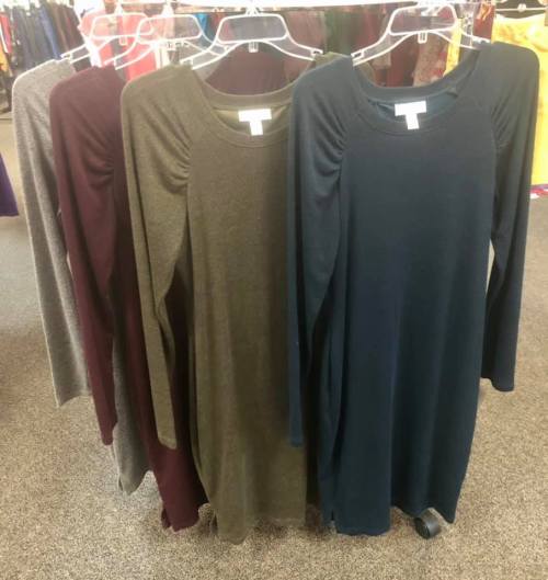 Five long-sleeve dresses in gray, burgundy, olive green, and dark green hanging on display in a clothing store.