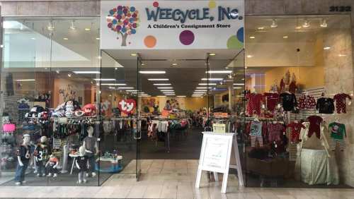 Exterior view of Weecycle, Inc., a children's consignment store, showcasing colorful clothing and toys through glass doors.