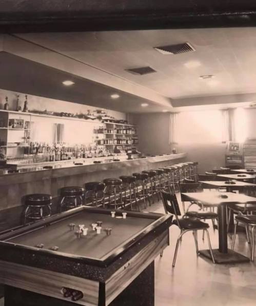 A vintage bar interior featuring a pool table, bar counter, and seating area with stools and tables.