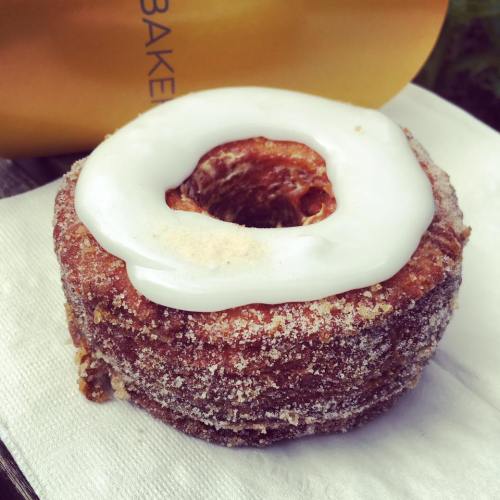 A delicious cronut topped with white icing, resting on a napkin with a yellow bag in the background.