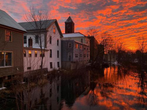 A vibrant sunset casts orange and pink hues over a river, reflecting buildings and a clock tower in the background.
