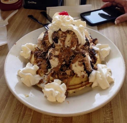 A large dessert featuring ice cream, whipped cream, chocolate sauce, and a cherry on top, served on a plate.