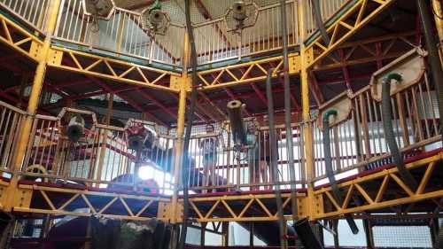 Colorful indoor playground structure with multiple levels, slides, and climbing features. Bright light shines through.