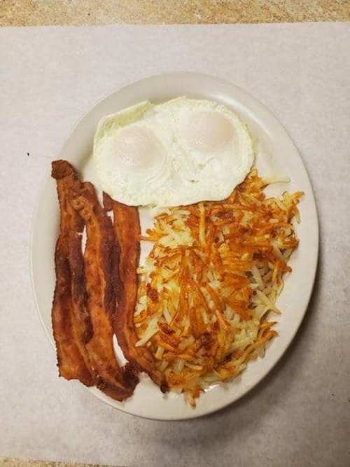 A plate with two fried eggs, crispy bacon strips, and golden hash browns on a white background.