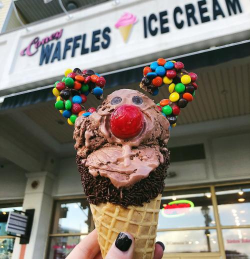 A whimsical ice cream cone shaped like a mouse, topped with chocolate ice cream, candy ears, and a cherry nose.