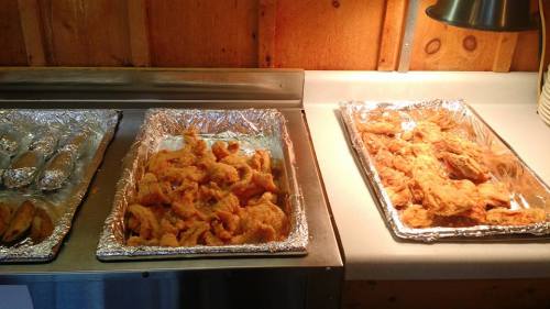 Two trays of fried food: one with shrimp and the other with chicken, both on a countertop with warm lighting.