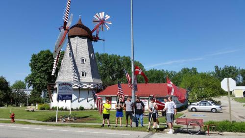 A group of people holding flags stands in front of a large windmill structure on a sunny day.