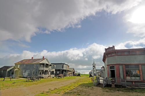 A historic western town with old buildings, a dirt road, and cloudy skies in the background.