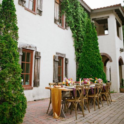 A beautifully set outdoor dining table with flowers, surrounded by a charming white building and lush greenery.