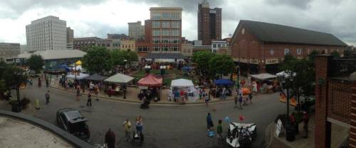 A bustling outdoor market with tents, vendors, and crowds under a cloudy sky in a city setting.