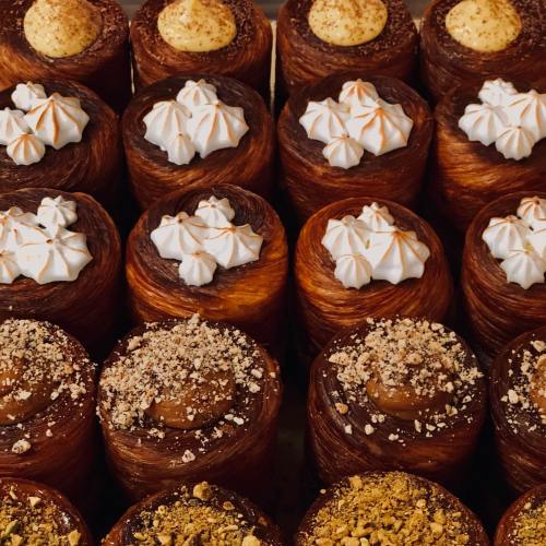 A close-up of beautifully decorated pastries with various toppings, including meringue and crushed nuts, arranged in rows.