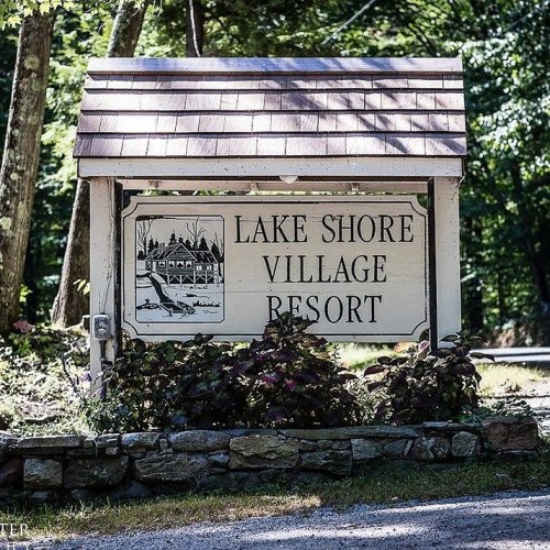 Sign for Lake Shore Village Resort surrounded by greenery and flowers, with a rustic wooden design.