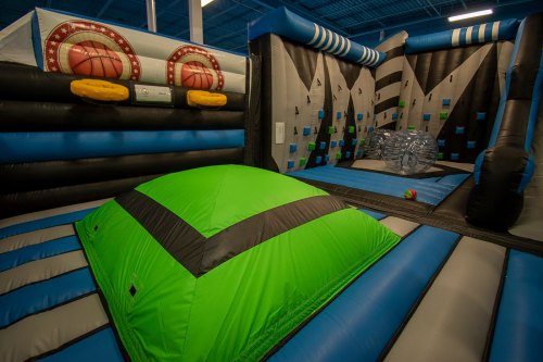 A colorful indoor bounce house with various inflatable structures, including a green hill and climbing wall.