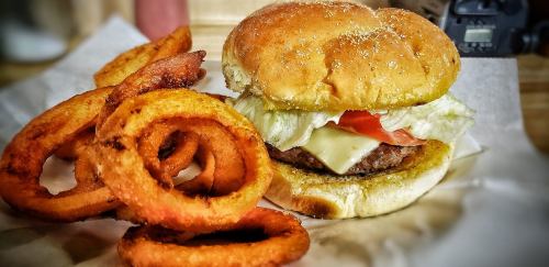 A juicy hamburger with lettuce, tomato, and cheese, served with crispy onion rings on the side.