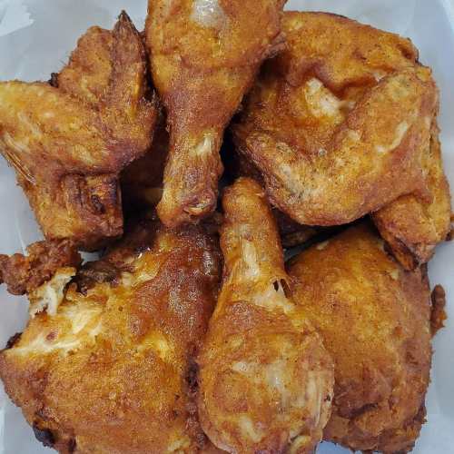 A close-up of crispy, golden-brown fried chicken pieces piled together on a white tray.