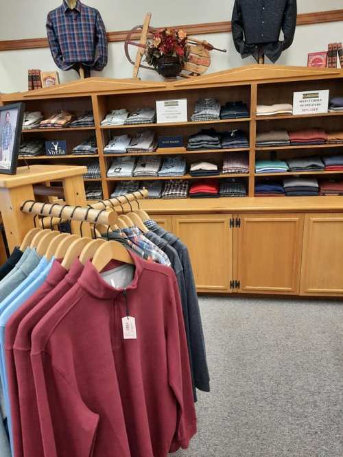 A clothing store display featuring various shirts and sweaters on hangers, with shelves of folded garments in the background.