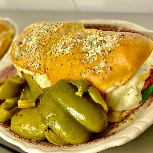 A hearty sandwich filled with melted cheese and peppers, served with a side of green peppers on a decorative plate.