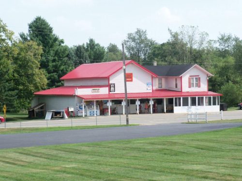 A two-story building with a red roof, featuring a storefront and surrounded by green grass and trees.