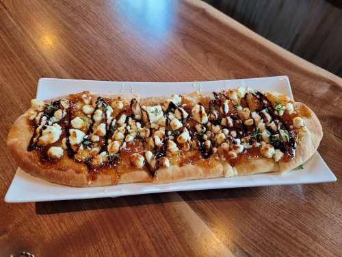 A flatbread topped with cheese, drizzled with balsamic glaze and garnished with herbs, served on a white plate.