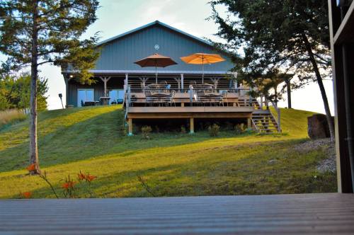 A hillside house with a deck, outdoor seating, and umbrellas, surrounded by trees and grassy landscaping.