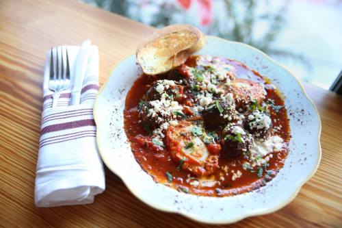 A plate of flavorful shakshuka with eggs, herbs, and a slice of toasted bread on a wooden table.