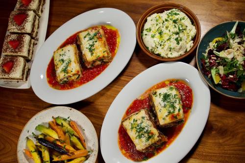 Two plates of lasagna on tomato sauce, accompanied by mashed potatoes, salad, and dessert on a wooden table.