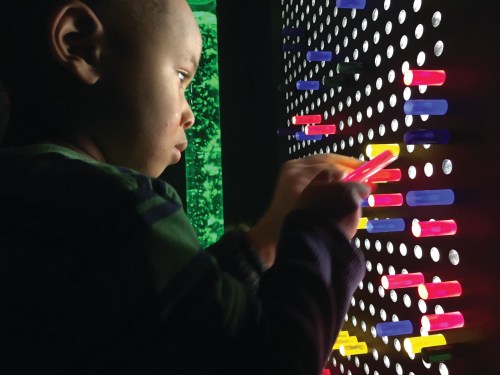 A child interacts with a colorful light display, focusing intently on placing pieces into a wall of holes.