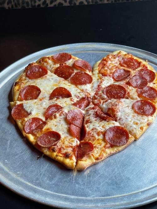 A heart-shaped pizza topped with pepperoni and melted cheese on a silver serving tray.