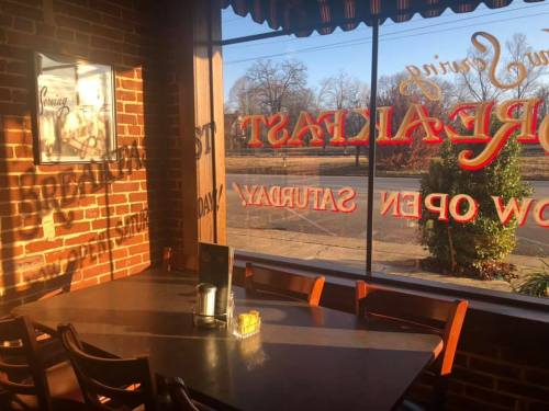 Cozy restaurant interior with a brick wall, empty table, and large window showing a sunny outdoor view.