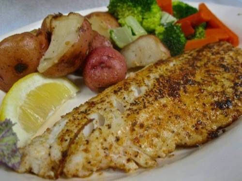 A plate featuring seasoned fish fillet, roasted red potatoes, and steamed broccoli and carrots, garnished with lemon.