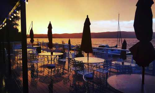 A lakeside patio with tables and umbrellas, reflecting a vibrant sunset over the water.