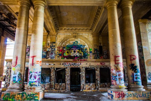 Abandoned building interior with tall columns, graffiti-covered walls, and a sense of decay and neglect.