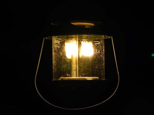 A glowing lantern with two bulbs, surrounded by darkness, casting a warm light.