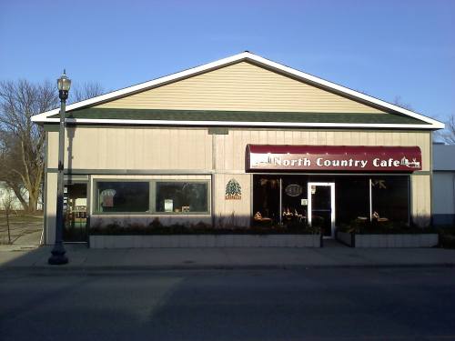 Exterior of North Country Café, featuring a sign, large windows, and a light post in front under a clear blue sky.