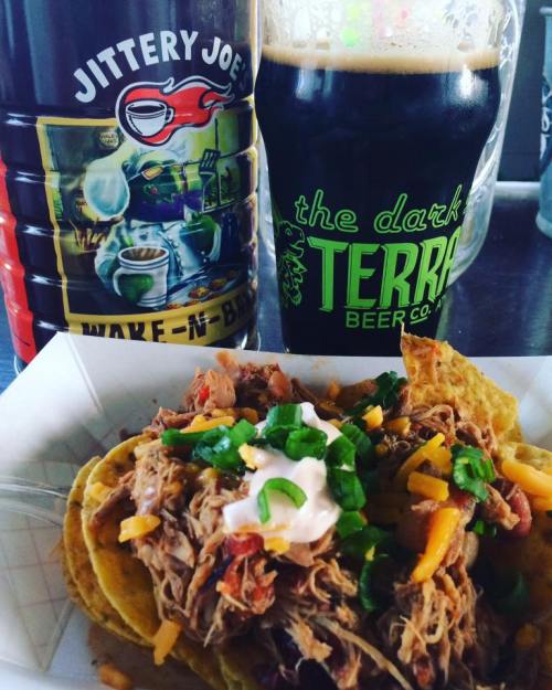 A plate of nachos topped with pulled pork, cheese, and green onions, alongside a dark beer and a coffee can.