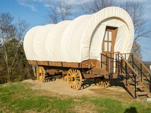 A covered wagon with a white canvas top, wooden wheels, and a staircase, set against a natural landscape.