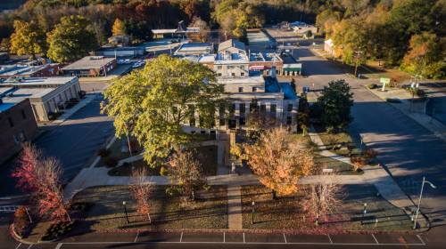 Aerial view of a town square with trees in autumn colors and buildings in the background.