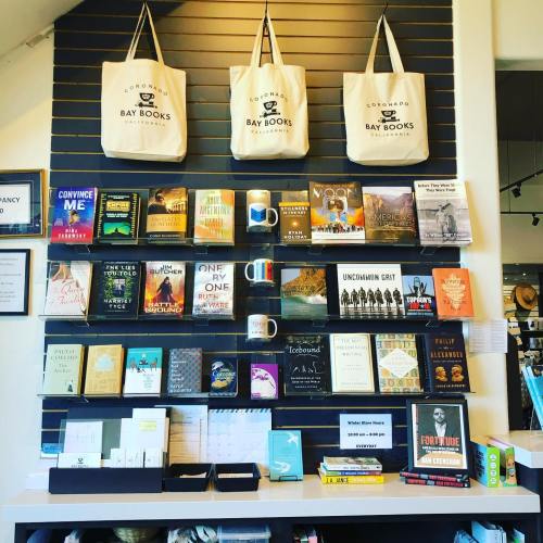 A cozy bookstore display featuring books on shelves, tote bags hanging above, and a welcoming reading area.