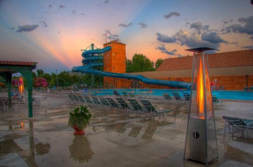 A water slide towers over a pool area at sunset, with lounge chairs and a heater in the foreground.