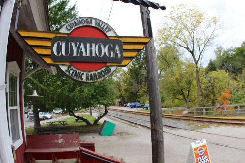 Sign for Cuyahoga Valley Scenic Railroad, with a view of a train track and trees in the background.