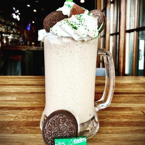 A frosty mug filled with a creamy dessert drink, topped with whipped cream, mint, and chocolate cookies.