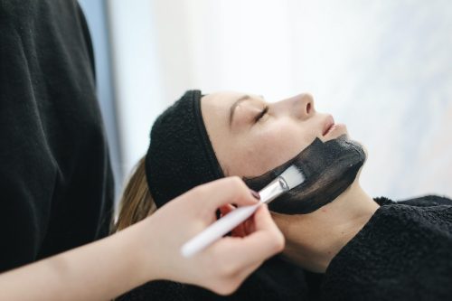 A woman receiving a facial treatment with a black mask being applied to her face.