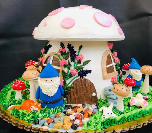 A whimsical cake shaped like a mushroom house, decorated with gnomes, flowers, and colorful stones.