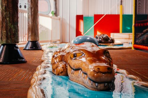 A playful indoor area featuring a large, colorful crocodile sculpture in a shallow blue pool.