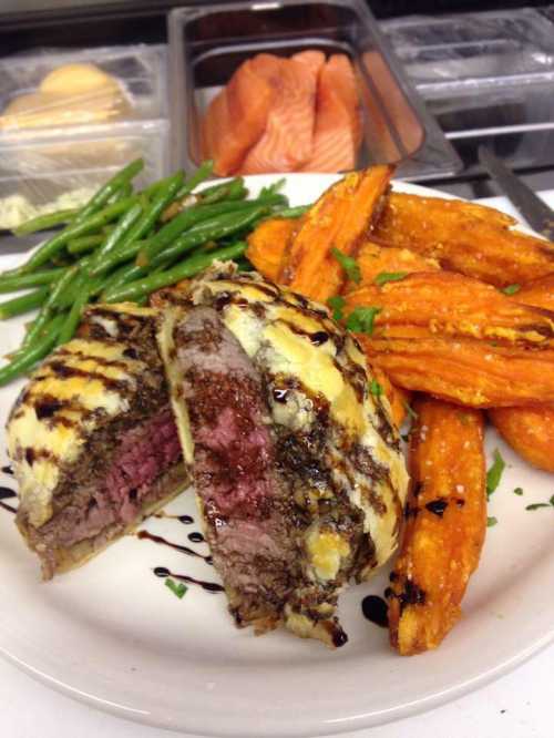 A plate featuring sliced steak, sweet potato fries, and green beans, drizzled with sauce and garnished with herbs.