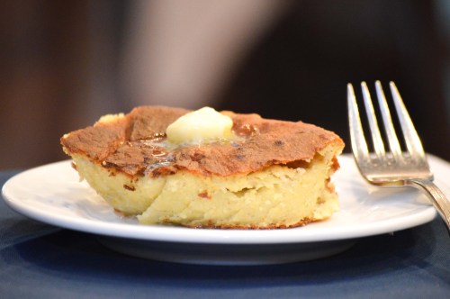 A slice of fluffy cornbread topped with a pat of butter on a white plate, with a fork beside it.